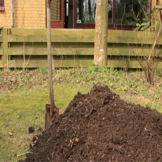 a large pile of dark brown compost mulch in a garden with a shovel