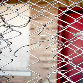 damaged chicken wire fence with red door in background